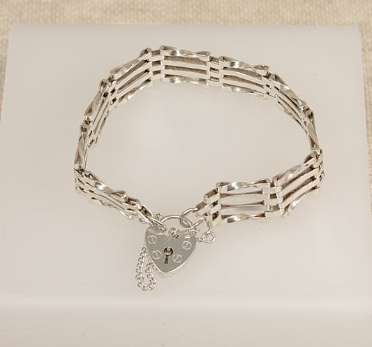 Silver gate bracelet with a heart-shaped padlock clasp on a beige background
