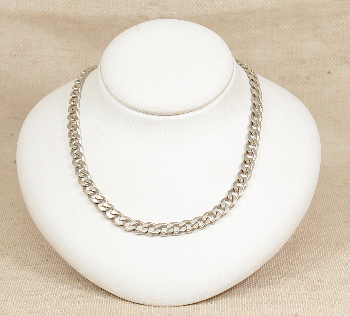 Silver chain necklace on a white bust against a beige background