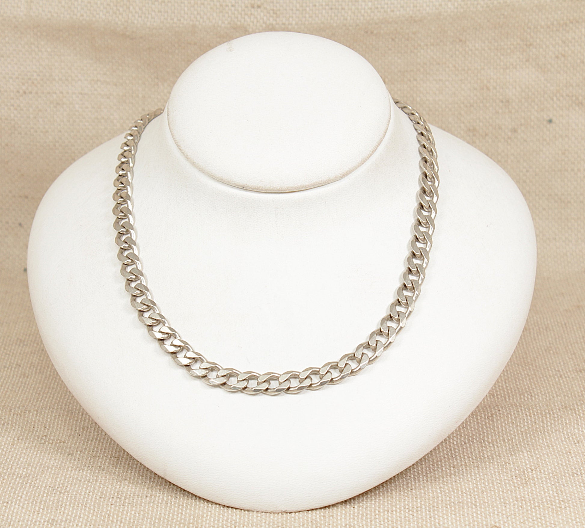 Silver chain necklace on a white bust against a beige background
