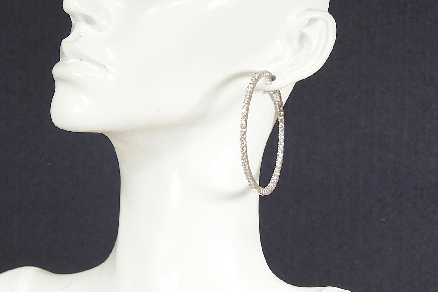 Silver hoop earrings on a white mannequin head against a black background