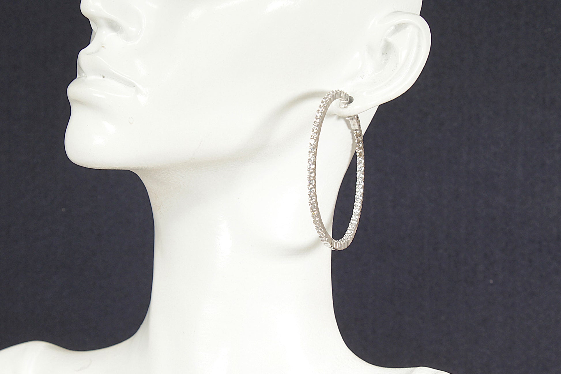 Silver hoop earrings on a white mannequin head against a black background