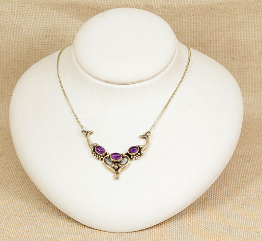 Silver art nouveau necklace with amethyst gemstones on a white stand against a beige background