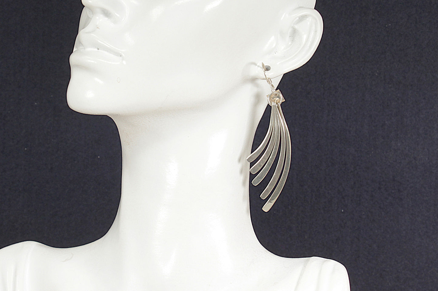 Silver earrings on a mannequin ear against a dark background