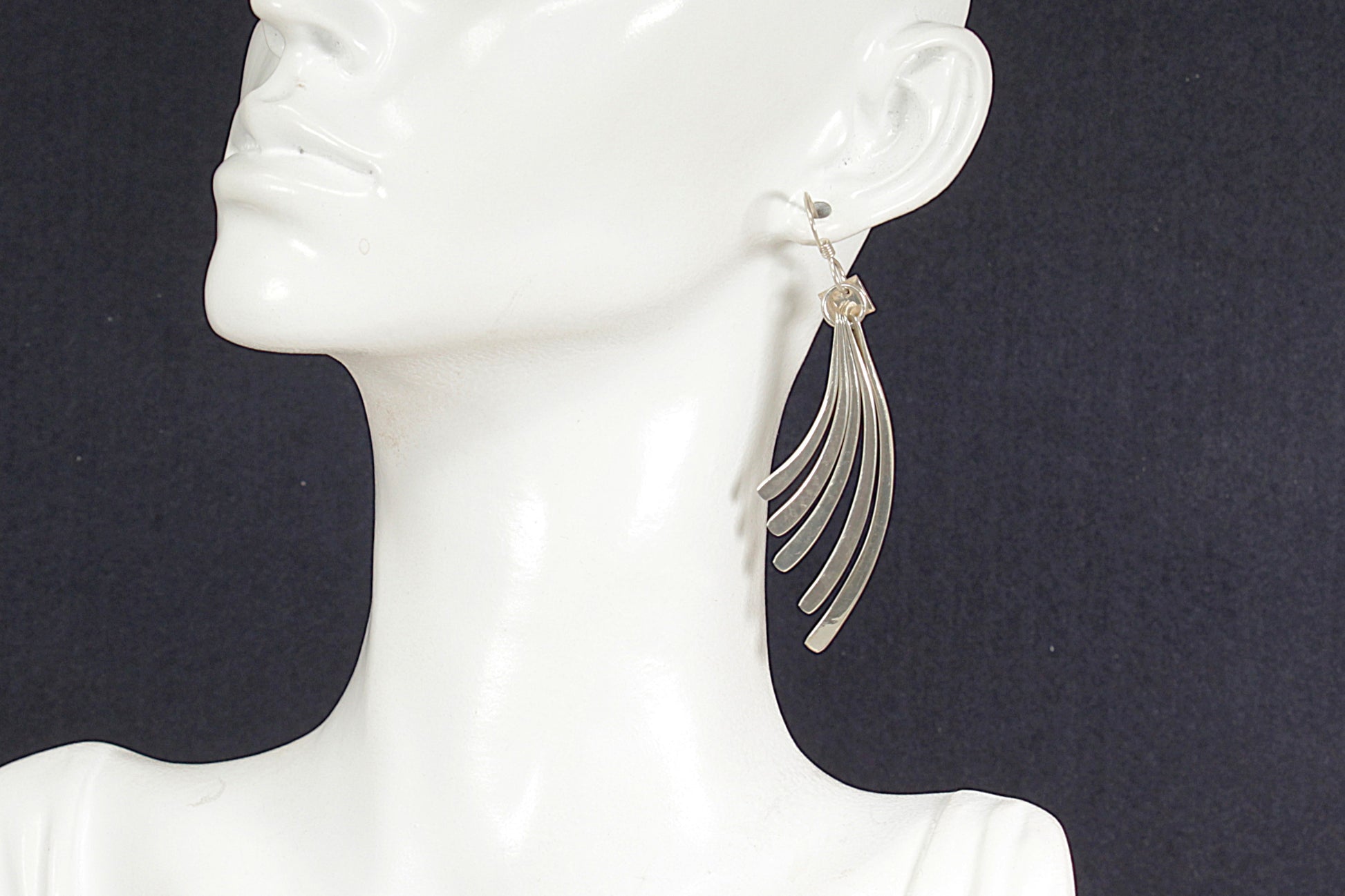 Silver earrings on a mannequin ear against a dark background