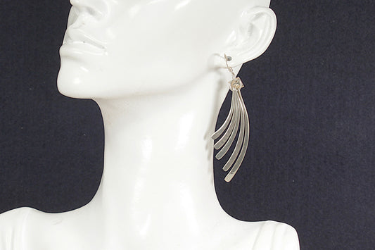 Silver earrings on a mannequin ear against a dark background