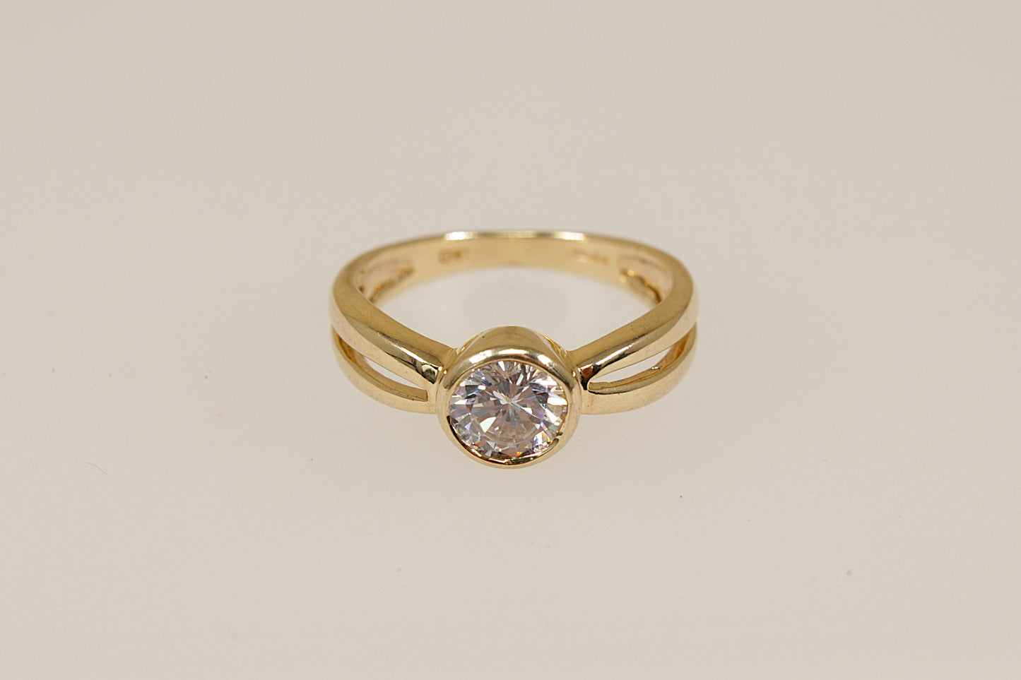Gold ring with a cubic zirconia diamond simulant gemstone on a beige background