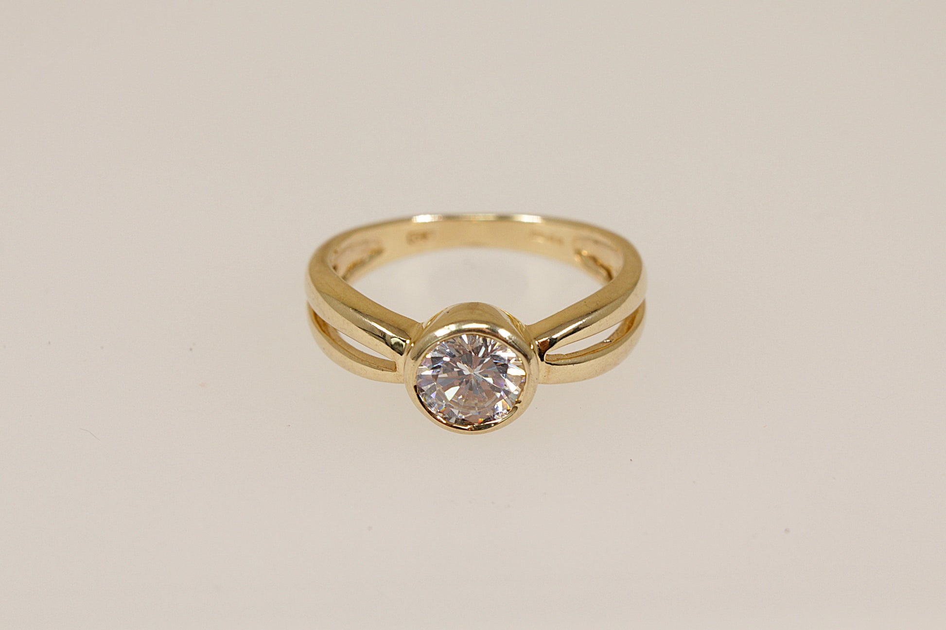 Gold ring with a cubic zirconia diamond simulant gemstone on a beige background