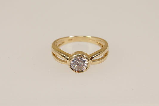 Gold ring with a cubic zirconia diamond simulant gemstone on a beige background