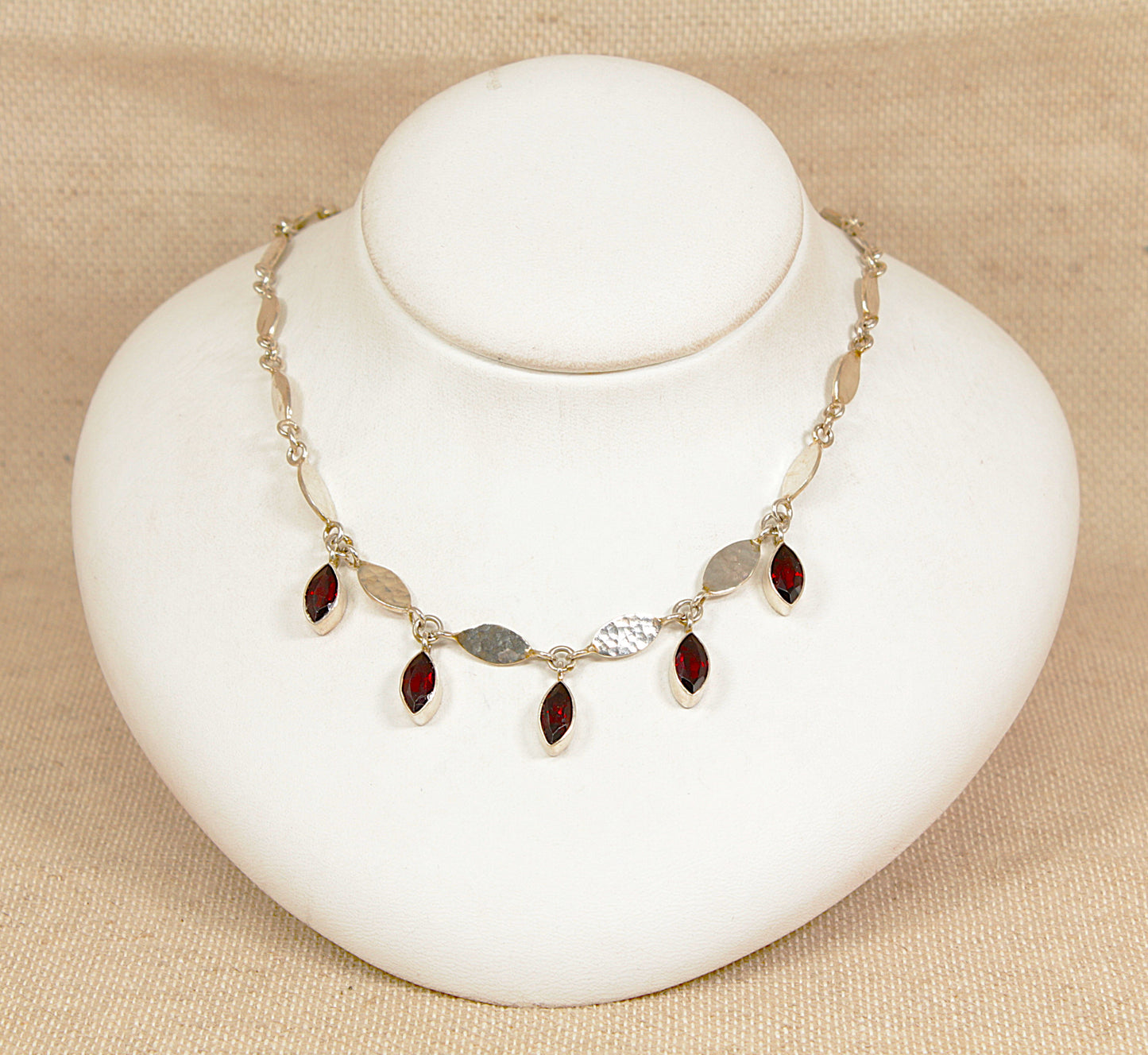 Necklace with red garnet gemstones on a white bust against a beige background