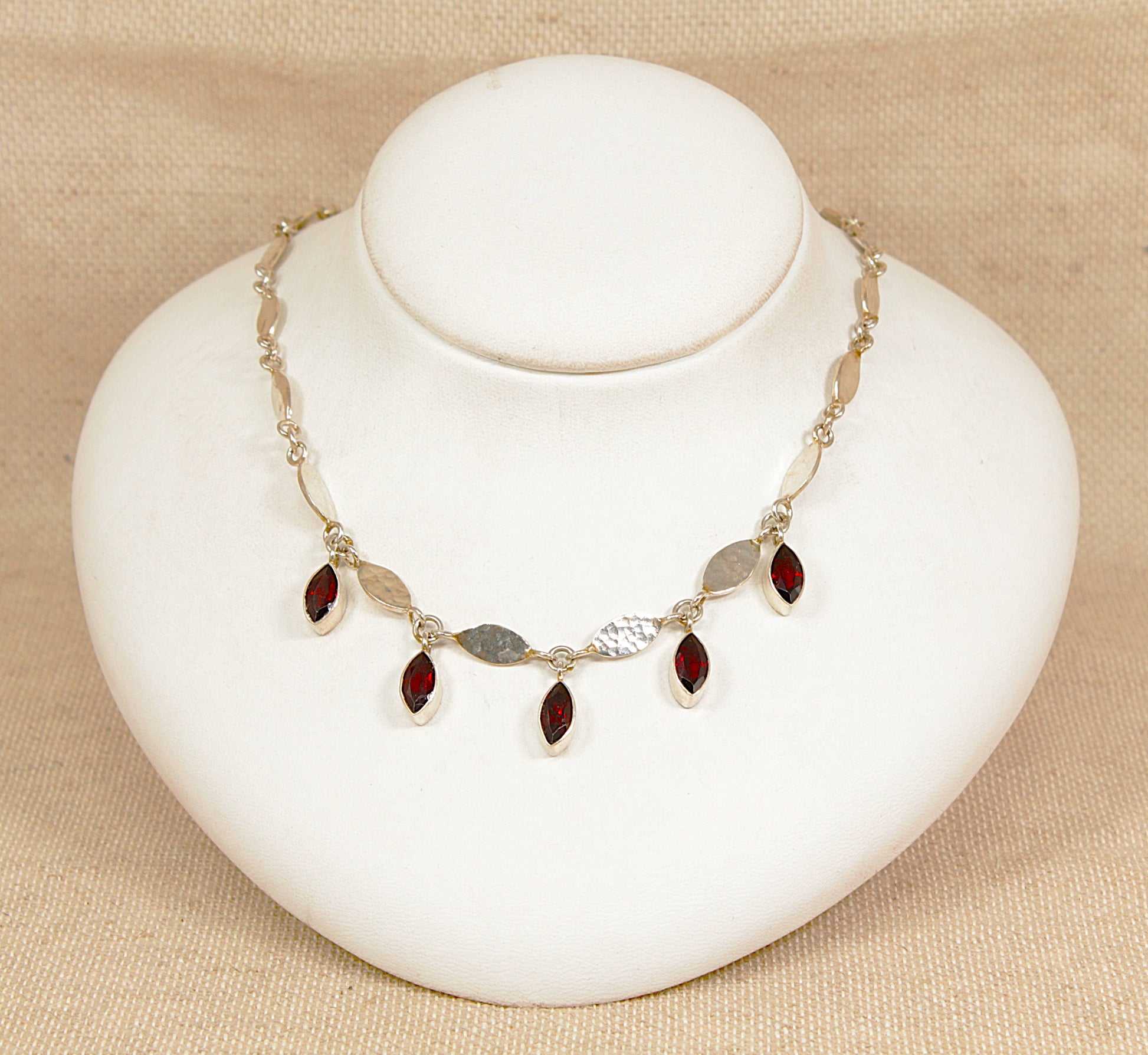 Necklace with red garnet gemstones on a white bust against a beige background