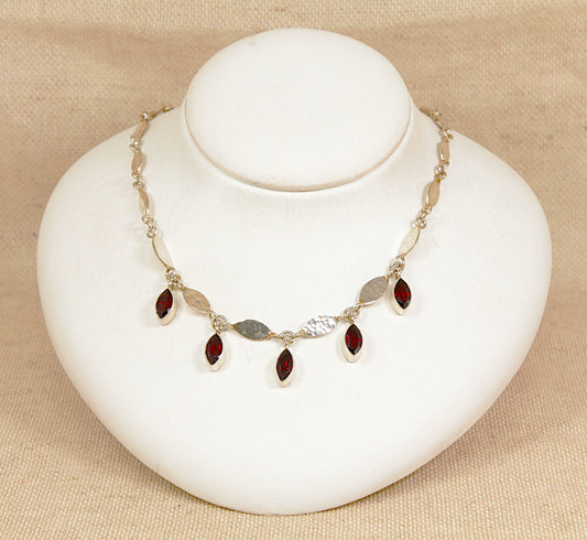 Necklace with red garnet gemstones on a white bust against a beige background