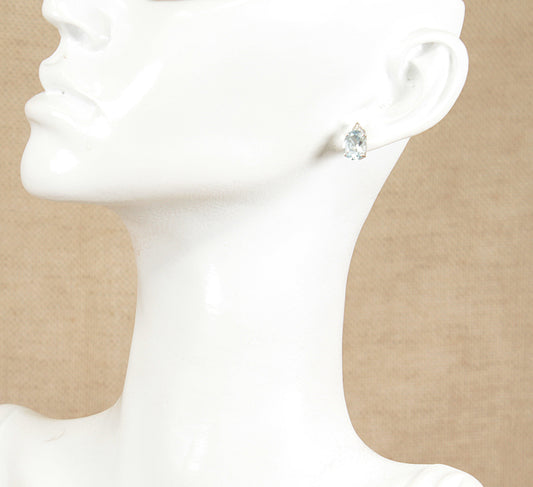Close-up of a aquamarine and diamond earring on a white mannequin ear against a beige background