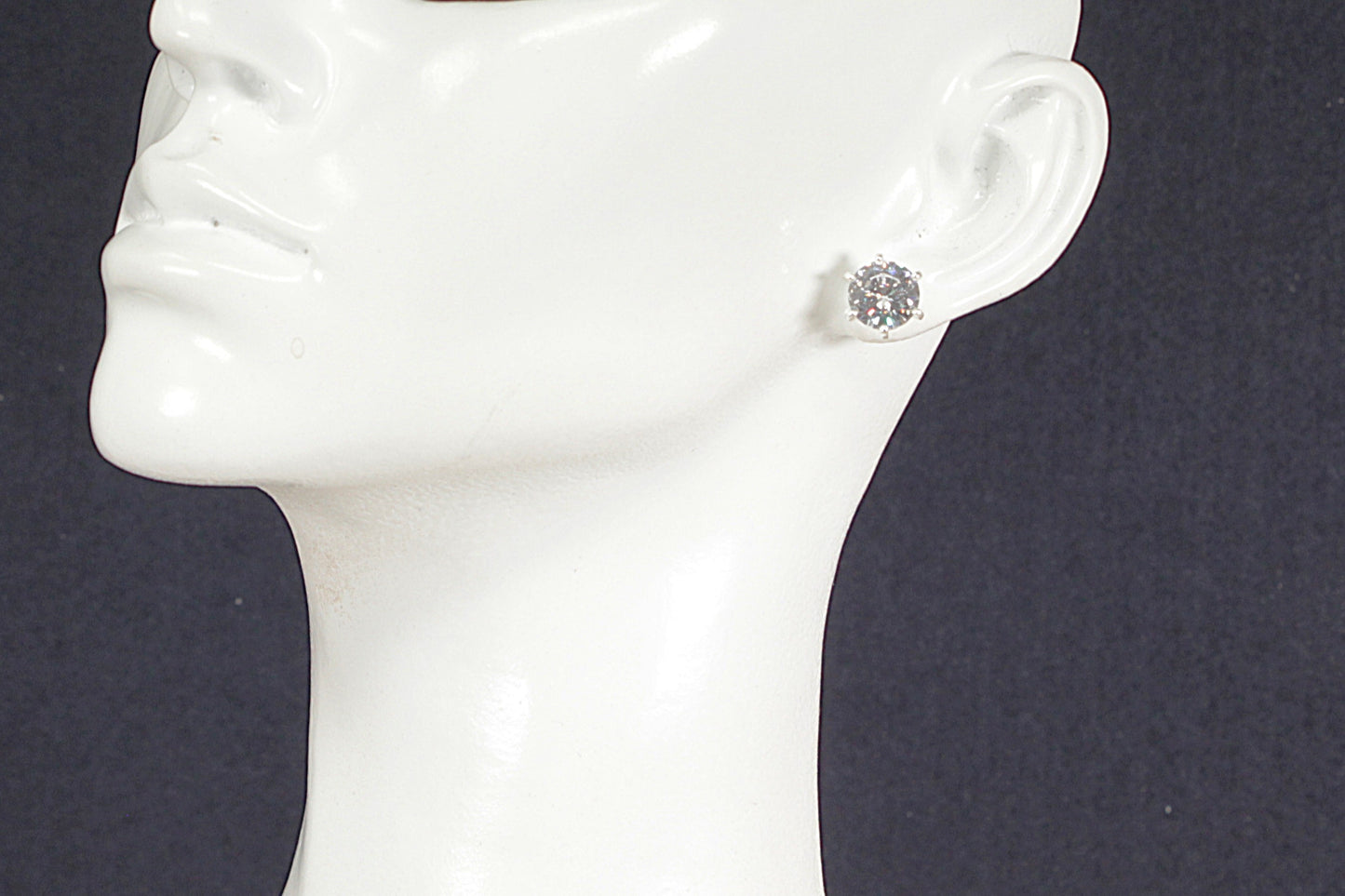 Silver earring on a mannequin ear against a dark background