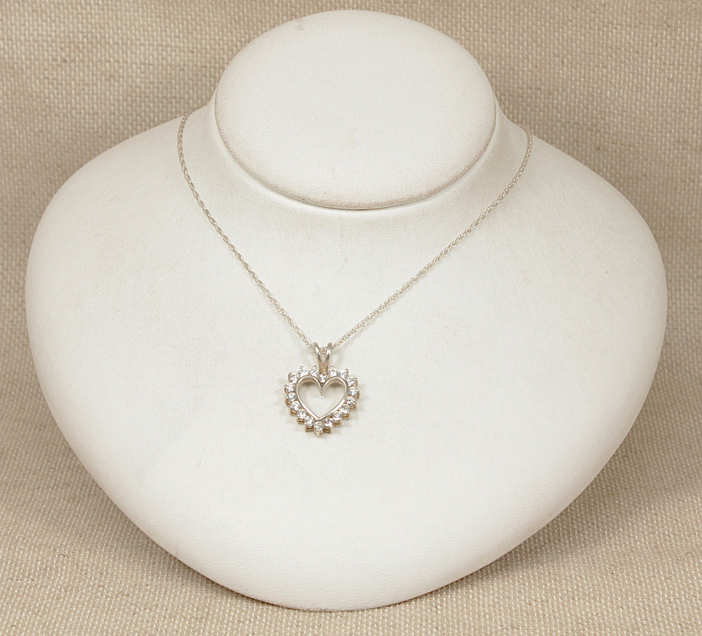Silver heart-shaped pendant necklace on a white round stand with a beige background