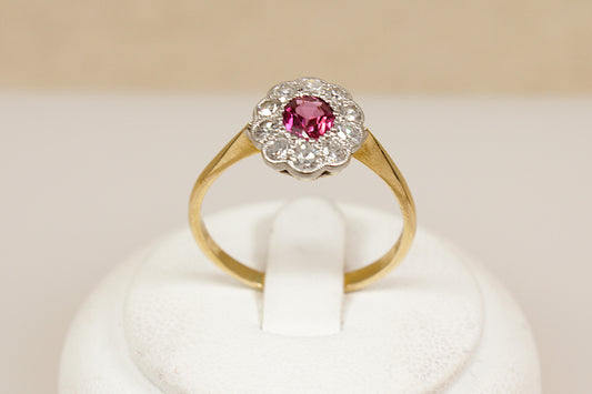 18ct ruby and diamond Gold ring with a halo of sparkling diamonds in a platinum mount on a white stand against a beige background