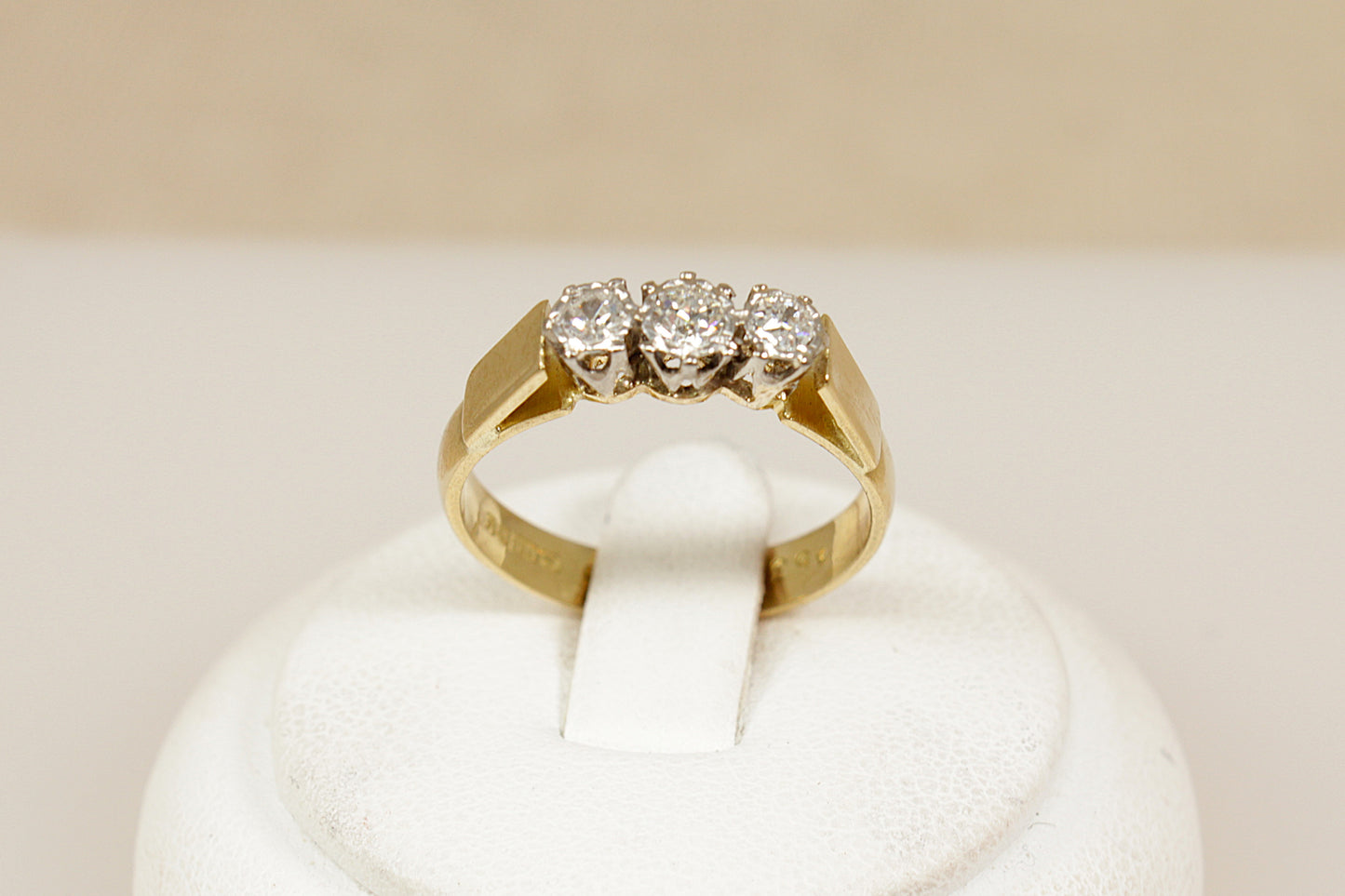 Gold ring with three diamonds on a white cushion against a beige background