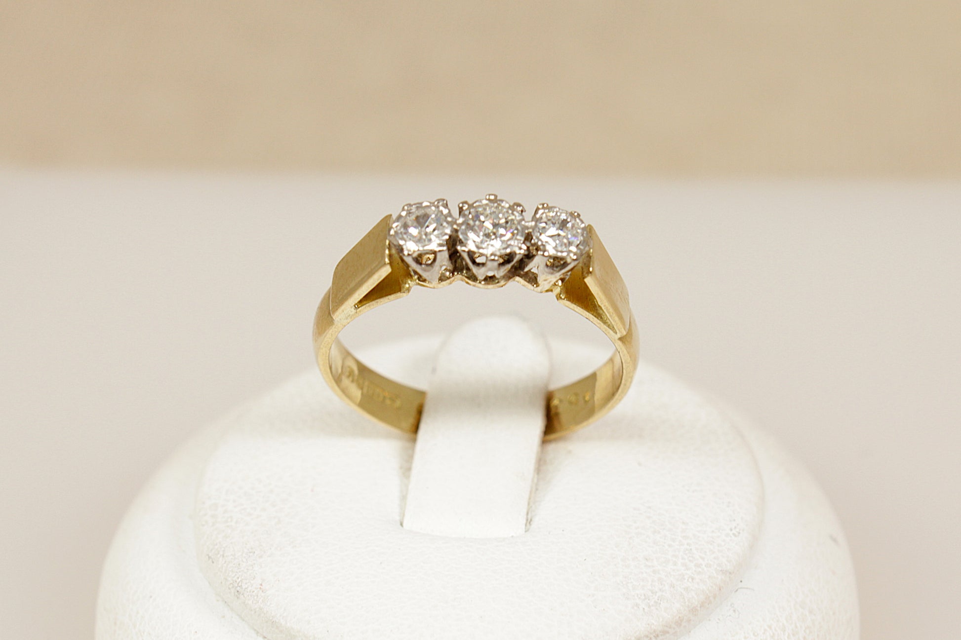 Gold ring with three diamonds on a white cushion against a beige background