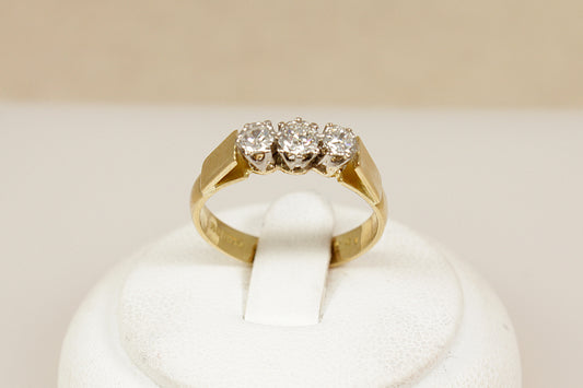 Gold ring with three diamonds on a white cushion against a beige background