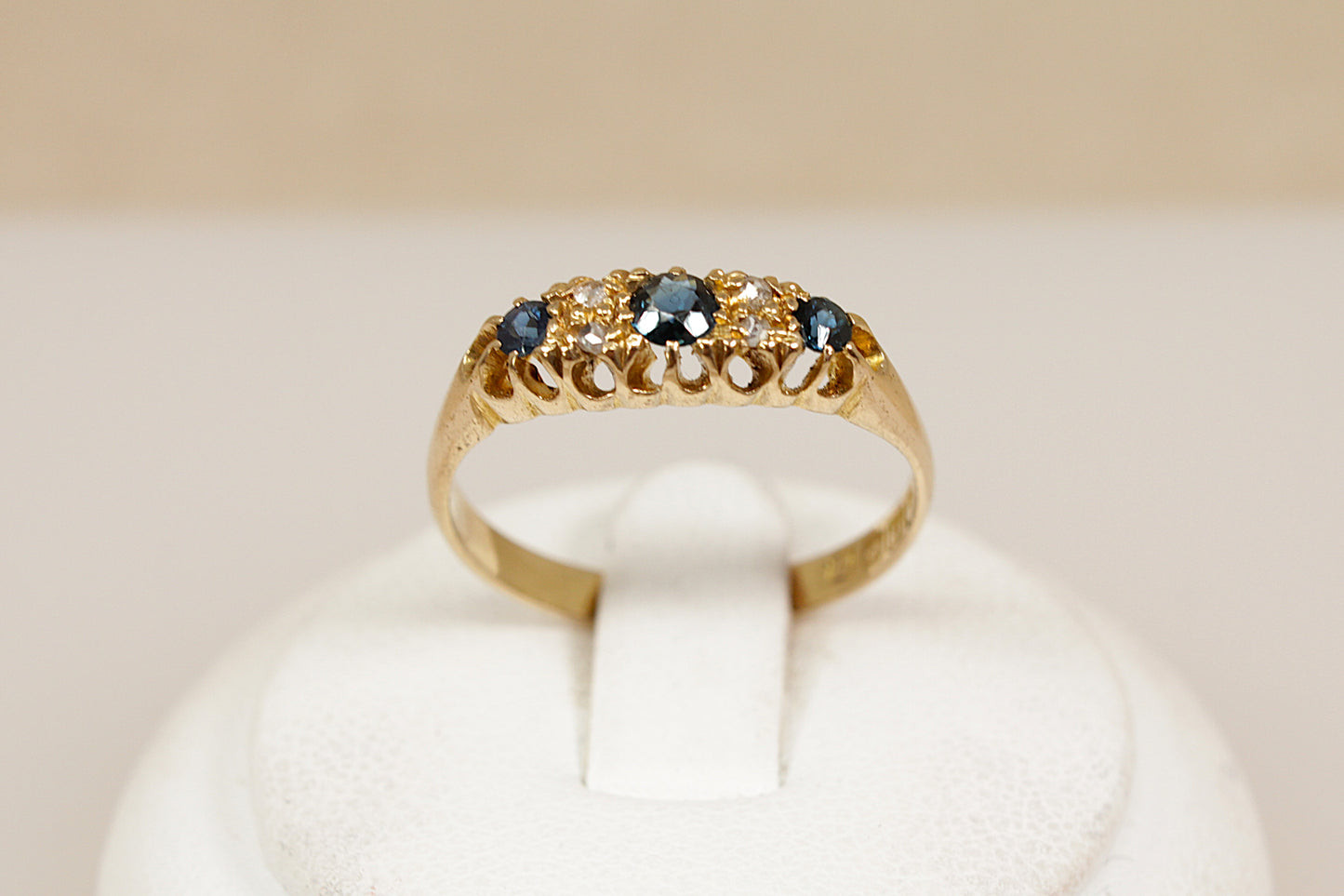 Antique 18ct sapphire and diamond  gold ring on a white cushion against a beige background