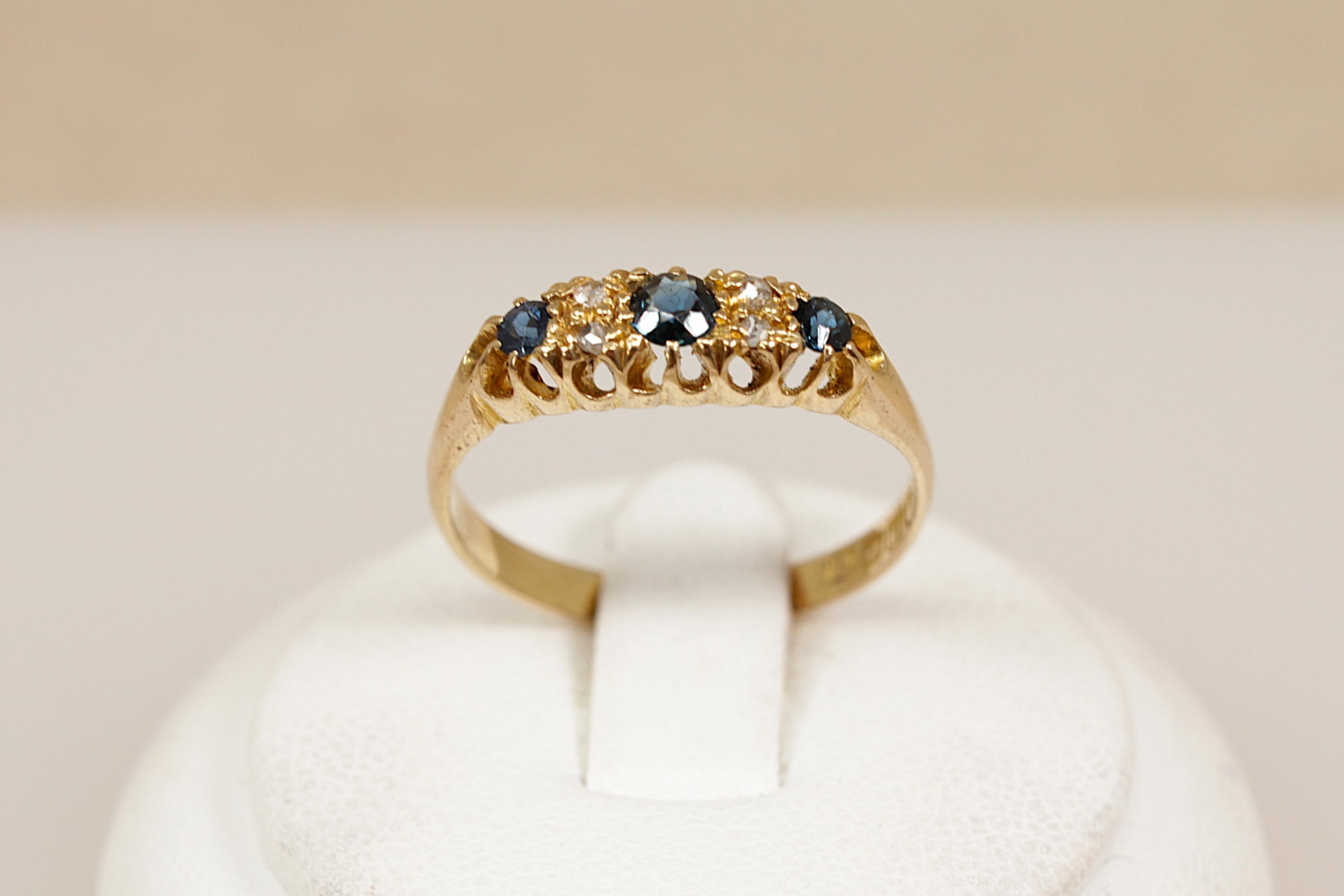 Antique 18ct sapphire and diamond  gold ring on a white cushion against a beige background