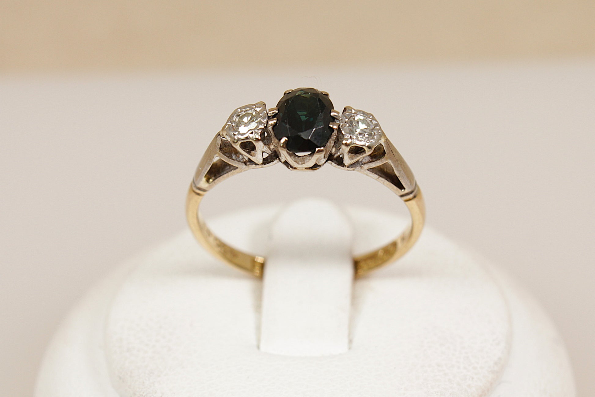 Gold ring with a blue sapphire gemstone and diamonds on a white stand.