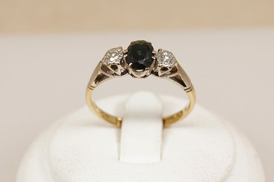 Gold ring with a blue sapphire gemstone and diamonds on a white stand.