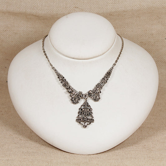Art Deco silver marcasite necklace with a pendant on a white stand against a beige background