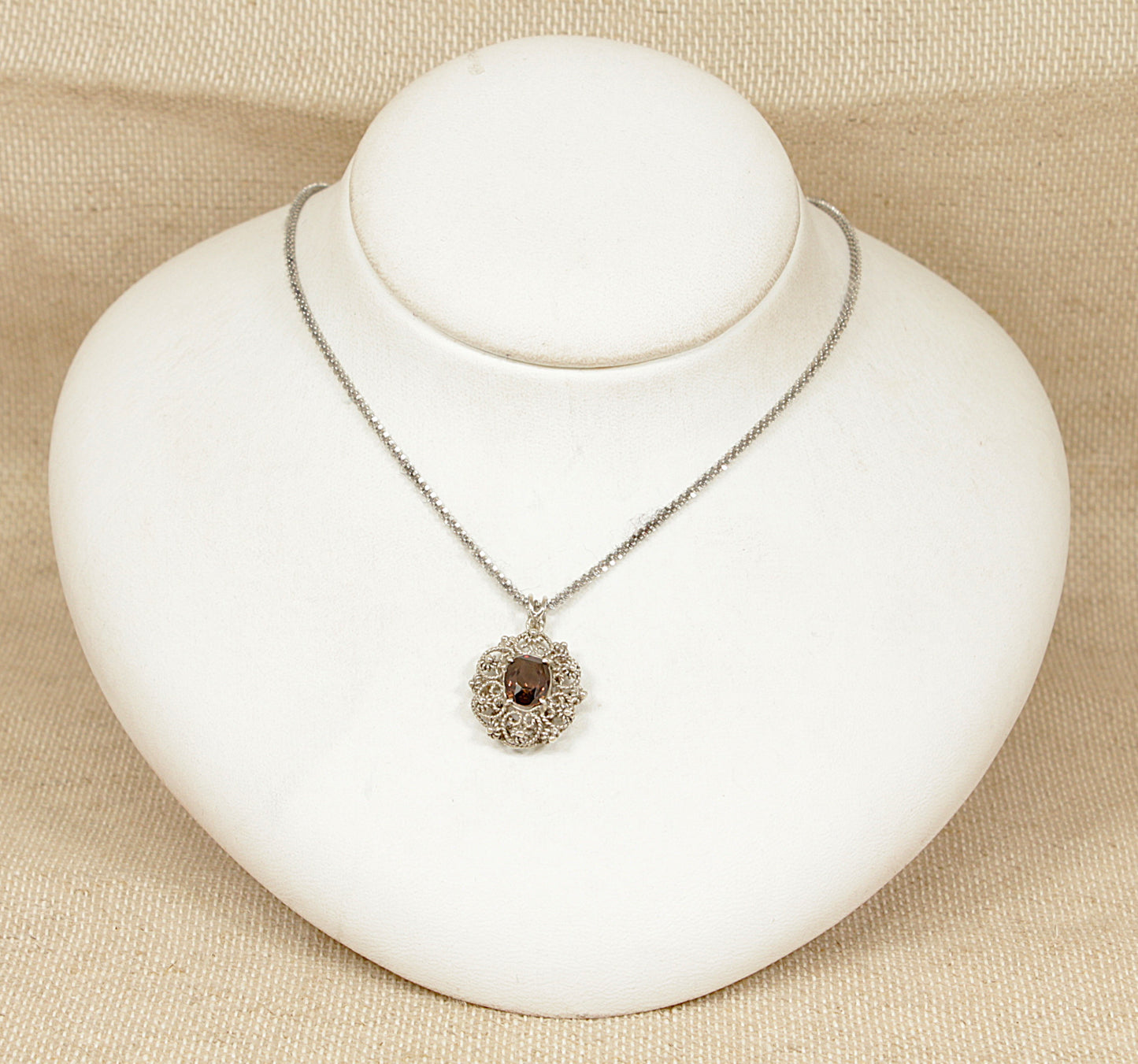 This beautifully hand-crafted Italian Silver pendant showcases a vibrant oval, faceted Golden Zircon, on a white bust with a beige background.