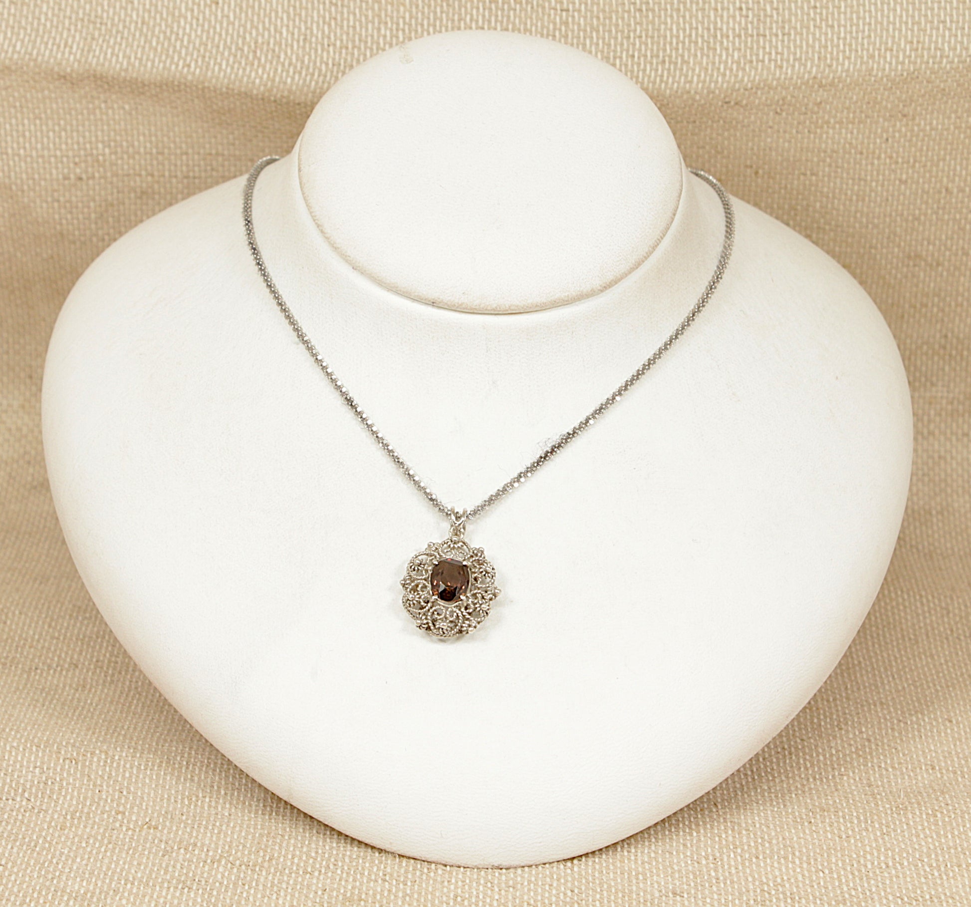 This beautifully hand-crafted Italian Silver pendant showcases a vibrant oval, faceted Golden Zircon, on a white bust with a beige background.