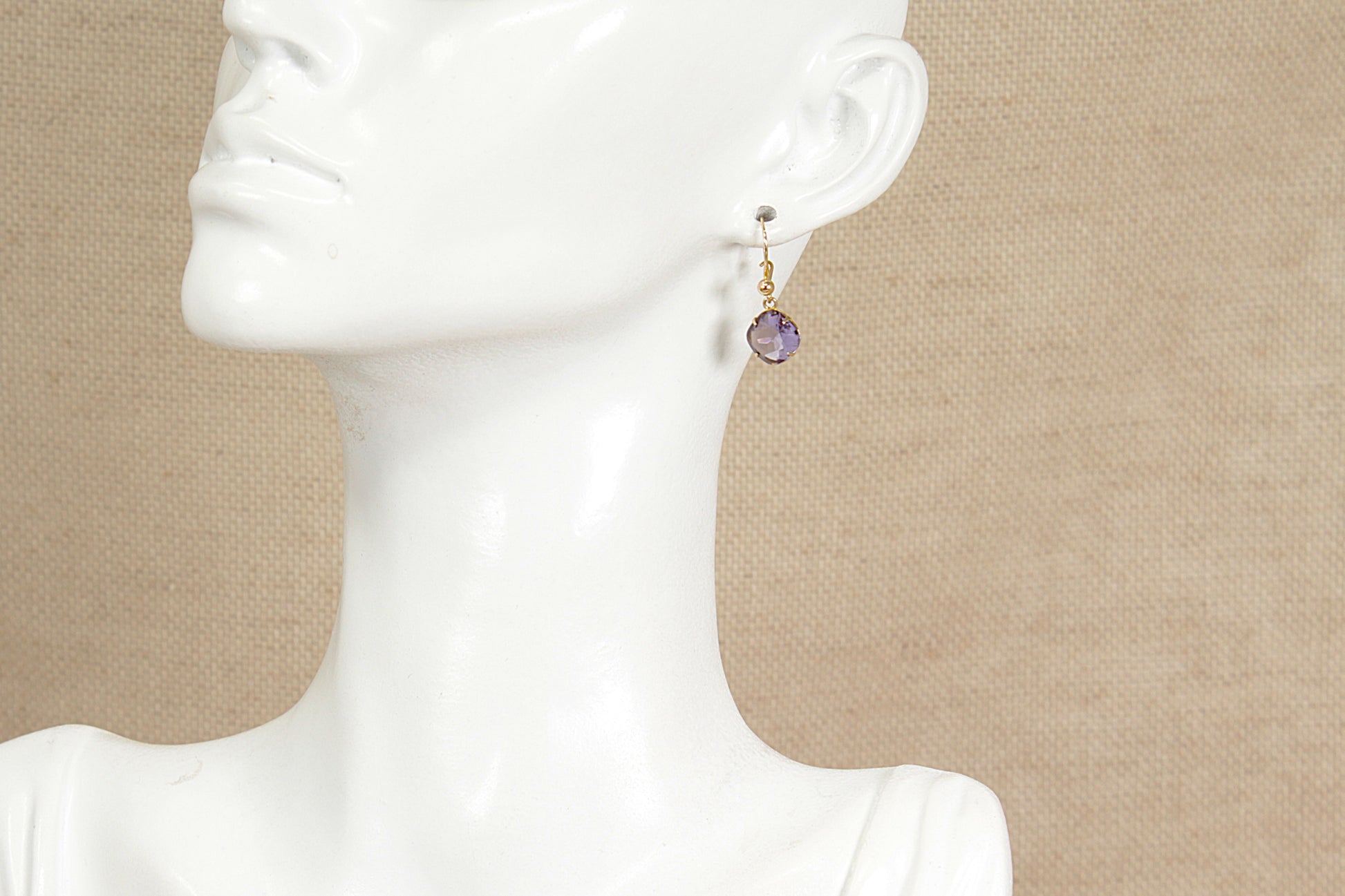 Gold amethyst earring on a mannequin with a beige background