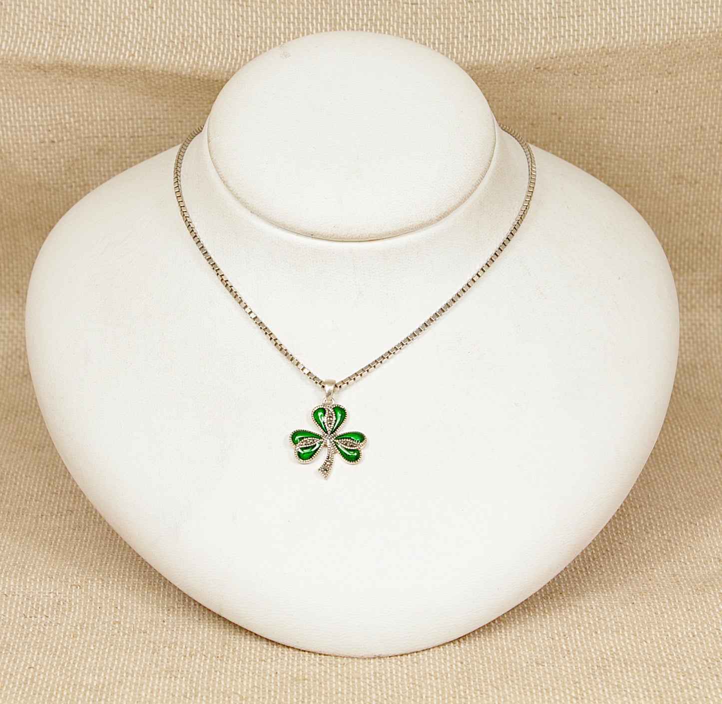 Irish green shamrock pendant  necklace on a white stand with a beige background