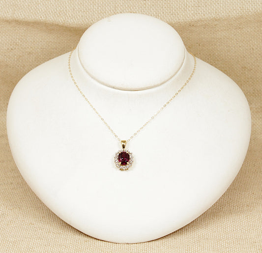 Gold necklace with a red almandine garnet gemstone surrounded by a halo of white topaz gemstones pendant on a white mannequin bust against a beige background