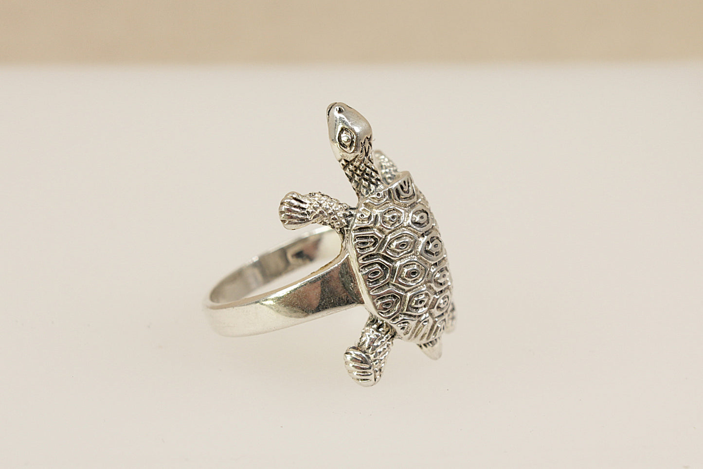 Silver turtle-shaped ring on a beige background