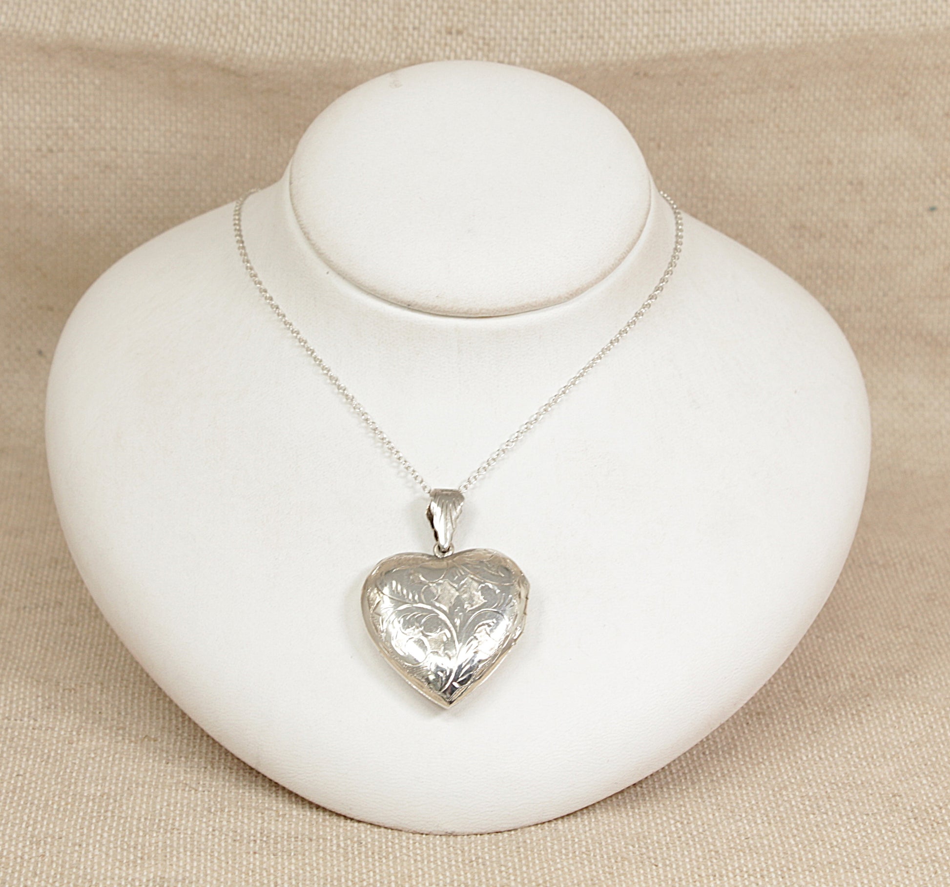 Silver heart-shaped locket on a white stand with a beige background