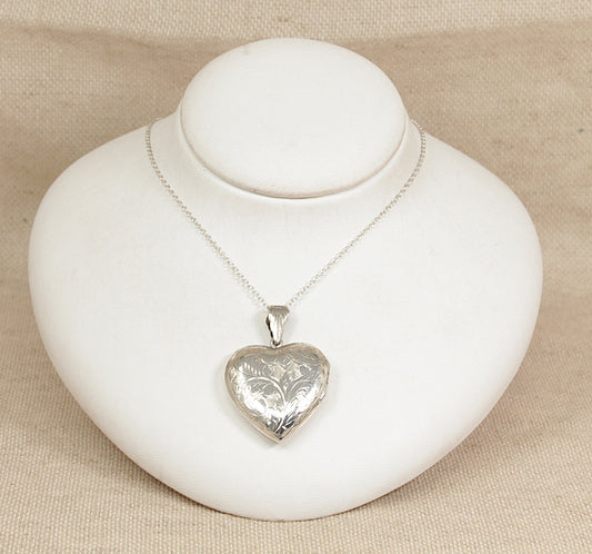 Silver heart-shaped locket on a white stand with a beige background