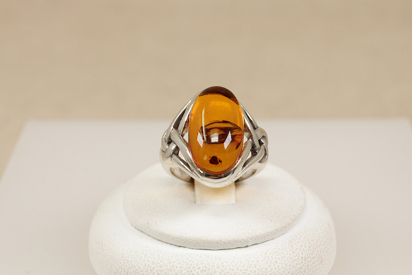 Silver ring with a amber gemstone on a white stand against a beige background