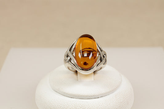 Silver ring with a amber gemstone on a white stand against a beige background