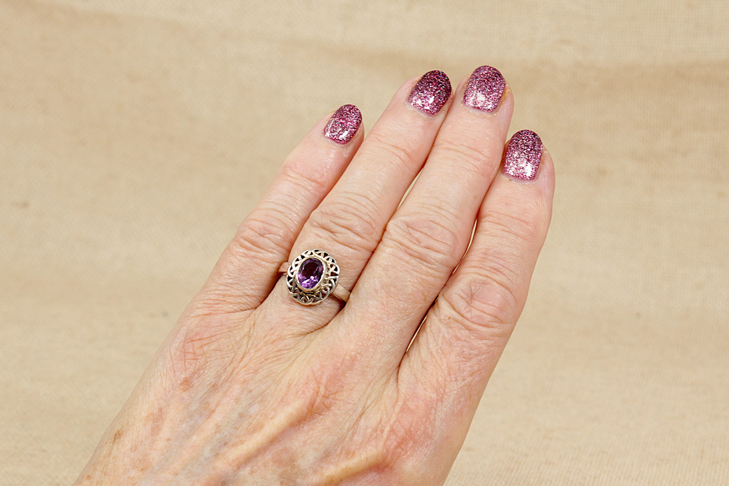 Hand wearing a ring with a purple amethyst gemstone on a beige background