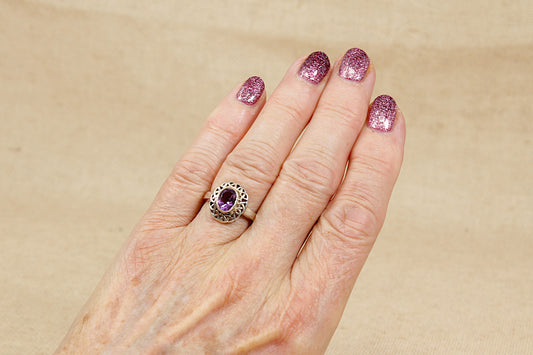 Hand wearing a ring with a purple amethyst gemstone on a beige background