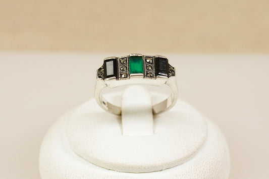 Silver art deco ring with green gemstone on a white stand against a beige background