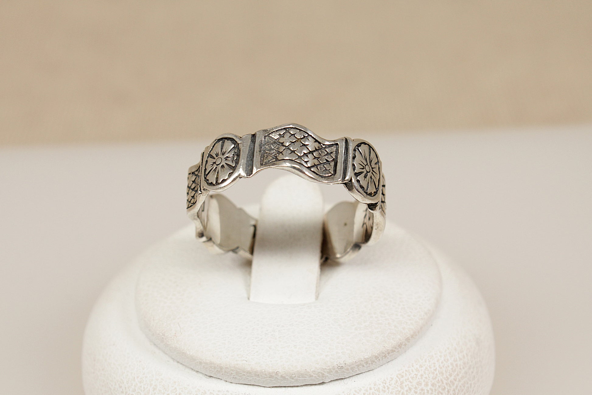 Silver ring with intricate design on a white stand against a beige background