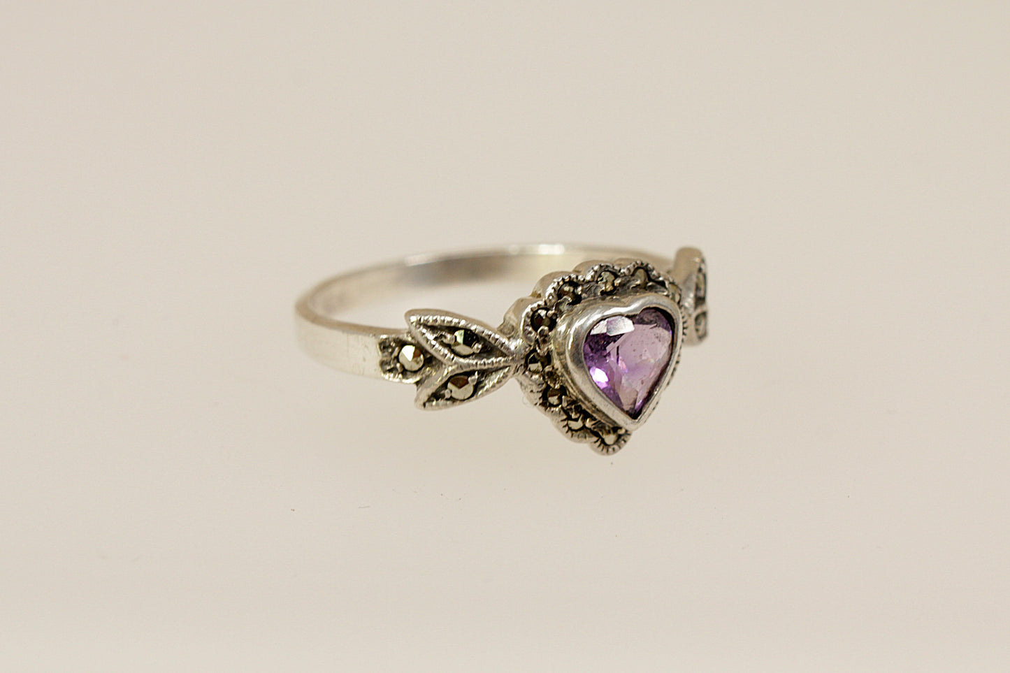 Silver ring with a heart-shaped purple amethyst and marcasite gemstones on a beige background