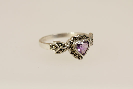 Silver ring with a heart-shaped purple amethyst and marcasite gemstones on a beige background