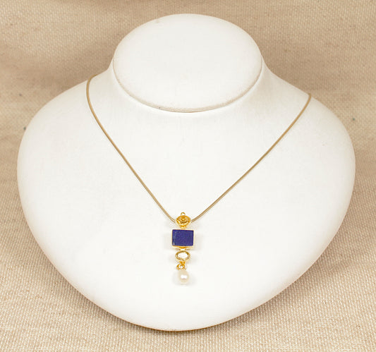 Gold plated silver necklace with a blue pendant on a white stand against a beige background