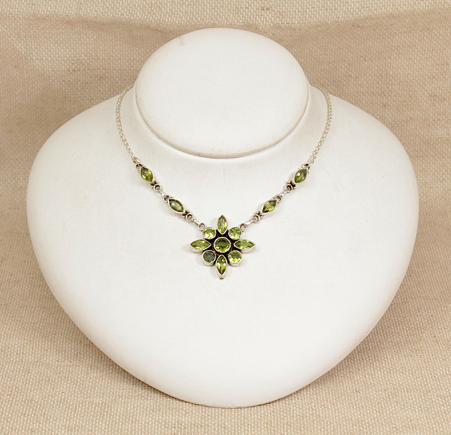 Necklace with green gemstones on a white stand against a beige background