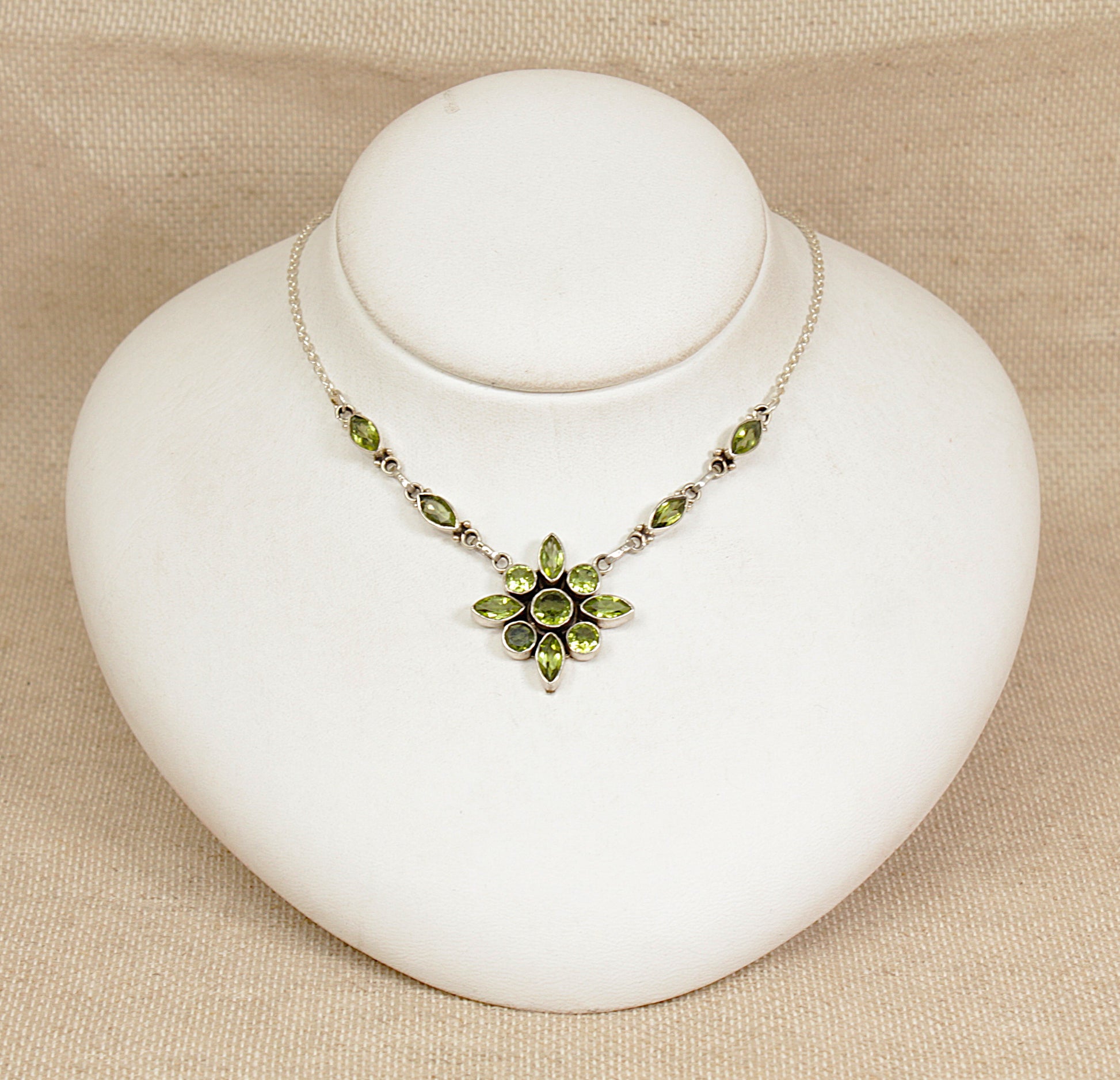 Necklace with green gemstones on a white stand against a beige background