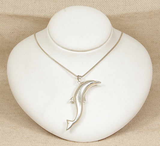 Silver snake chain necklace with a dolphin pendant on a white heart-shaped stand.