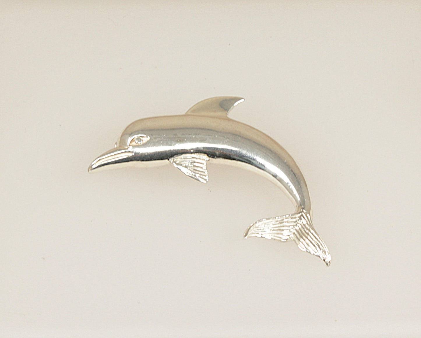 Silver dolphin figurine brooch on a light beige background