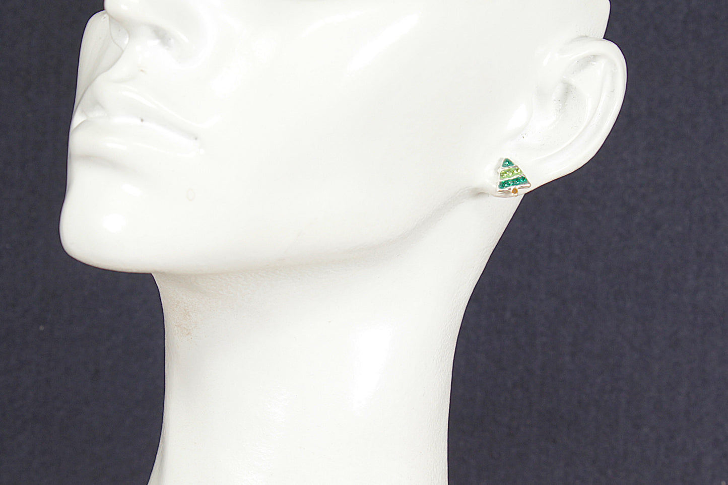 Christmas tree earring on a mannequin ear against a dark background