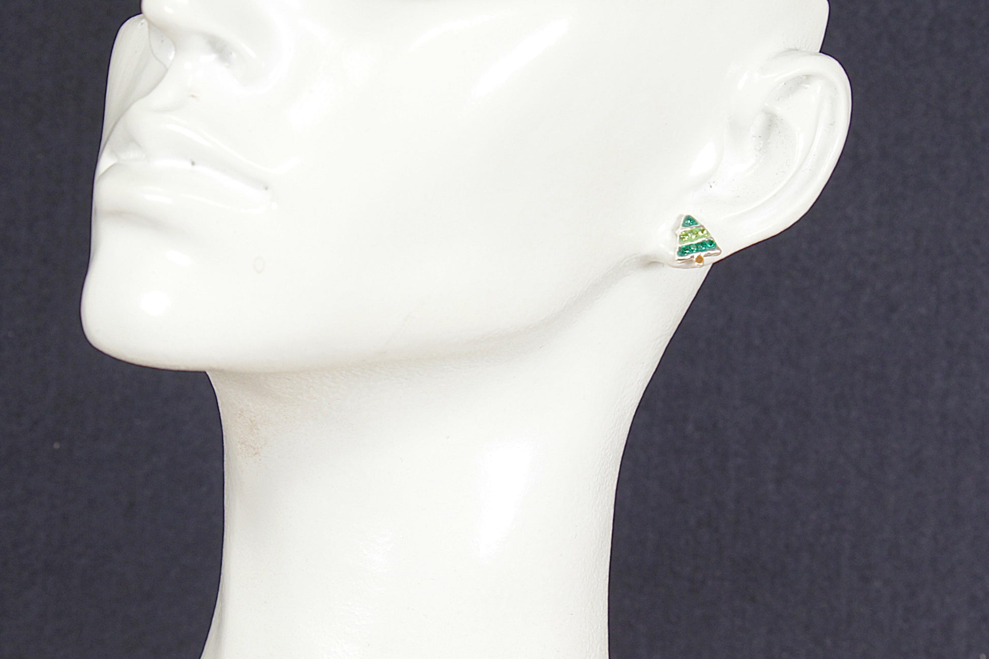 Christmas tree earring on a mannequin ear against a dark background